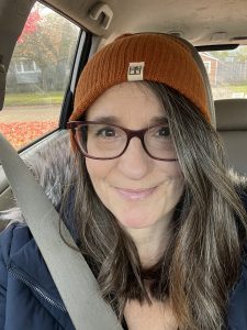 A photo of a white woman sitting in a car wearing an orange beanie.